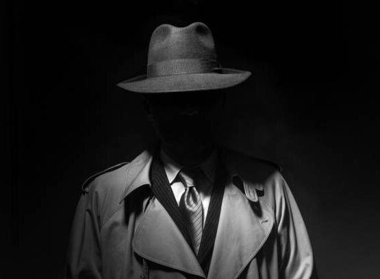 Man posing in the dark with a fedora hat and a trench coat, 1950s noir film style character